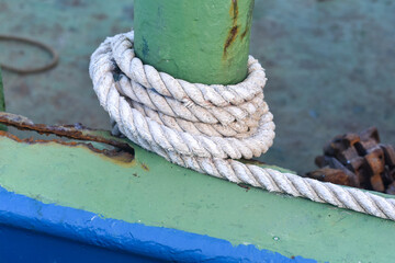 white rope on an iron pole. A thick white rope is wrapped around a green metal bollard, securing a...