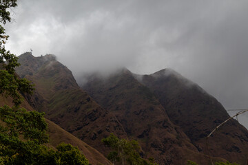 Dark cloudy sky hangs over rugged green and brown mountain landscape.