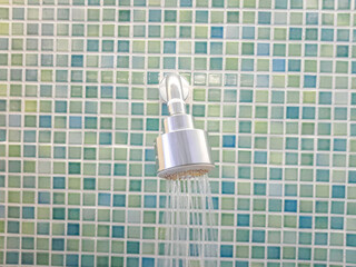 Modern Shower Head with Running Water Against Mosaic Tile Wall. A sleek metal shower head releasing...
