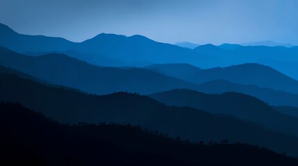 Fototapeta premium Layers of blue mountain ranges fading into the distance under a clear sky, creating a tranquil and serene natural landscape.