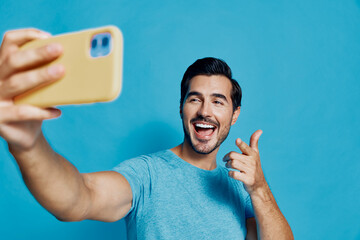 Cheerful smiling man taking selfie with smartphone against a bright blue background. Happy...
