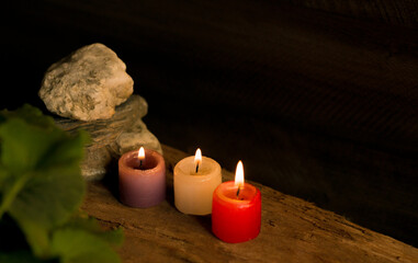 Velas encendidas de colores junto a piedras y hojas sobre superficie de madera en ambiente cálido...