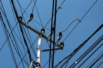 Tangled network of overhead power lines and cables against a clear blue sky.
