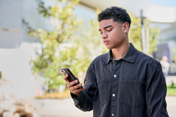 Young Dominican man with a clean taper fade haircut and a dark shirt looks intrigued while staring at his mobile phone screen. Casual indoor moment captured with natural curiosity and focus.