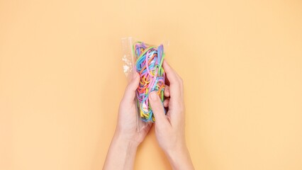 Hands Holding Colorful Rubber Bands in a Bag on a Beige Background, Crafting and DIY Concept