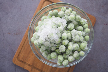 Frozen green peas in a glass bowl on a wooden cutting board