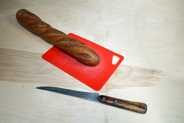 Rye baguette and kitchen knife on plastic red cutting board.