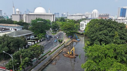 Aerial image of heavy equipment excavator dredging mud from river flow in the middle of city street