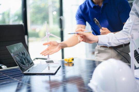 Engineers discuss solar panels and turbines in office, working on clean energy design, sustainable power,