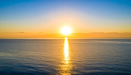 Naklejka premium Sunset over calm ocean water with golden reflection and clear sky creating peaceful and warm atmosphere