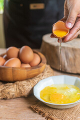 Detail of broken egg falling into pan as woman holds eggshell in both hands