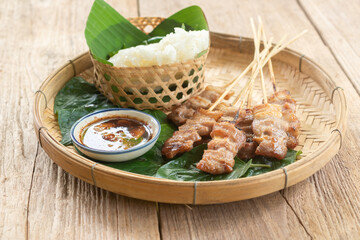 Thai style grilled pork and steamed sticky rice With Jaew dipping sauce on a wooden floor