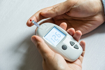 Woman's hands checking diabetes and hyperglycemia with digital blood sugar meter. Healthcare and...