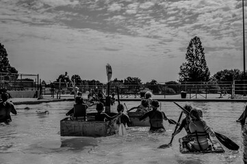 Two small kids paddling a cardboard boat in a race in a pool 