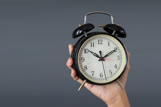 Hand Showing Classic Alarm Clock Against Grey Background