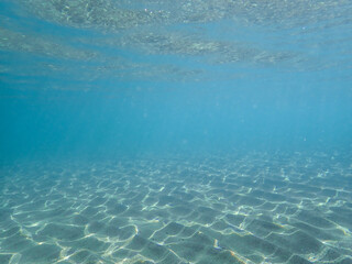 Obraz premium Dark blue ocean surface seen from underwater. Abstract waves underwater and rays of sunlight shining through, Sun light rays undersea deep, Underwater background with sea bottom, Mediterranean sea.