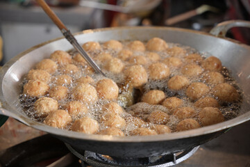 Meatballs are being deep-fried in hot oil, turning golden brown and crispy inside a large wok on a street food stall.