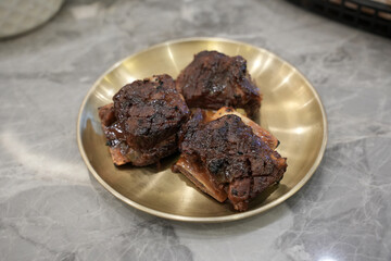 Grilled beef ribs are served on a golden plate, looking juicy and charred