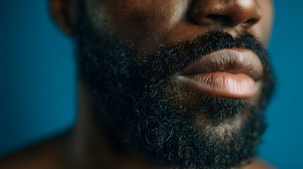 Closeup portrait of a black man s beard lips and skin against a blue background highlighting a morning skincare or grooming routine with a contemporary cinematic lighting setup