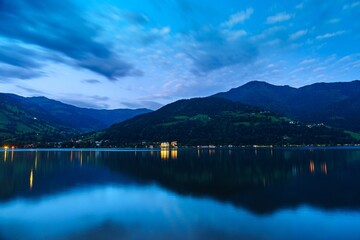 Discover the tranquil beauty of Lake Zell at dusk. Calm waters reflect ambient lights from lakeside...