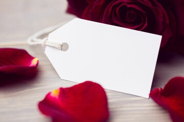 Flat illustration is showing white gift tag on tabletop with string, red rose petals, copy space