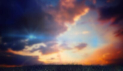 Sunset sky is showing multicolored clouds over lit grassy meadow in flat design with sun rays