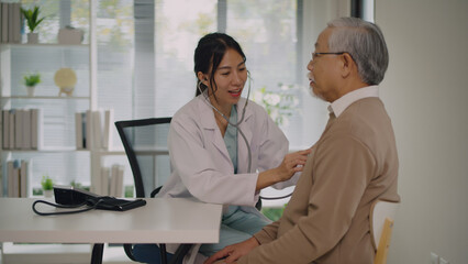 A caring female doctor in a lab coat uses a stethoscope to examine an elderly male patient in a...