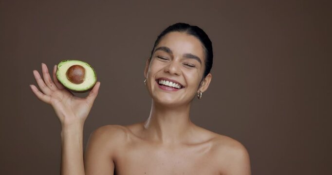 Face, skincare and woman with avocado, glow and natural cosmetic for anti aging, smile and wellness. Studio background, happy and person with fruit for dermatology, mockup space or treatment for skin