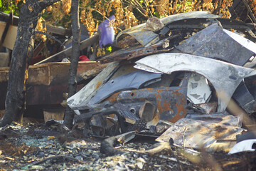 Consequences of heat and a person's careless attitude to safety rules: a view of burnt-out small business replacing auto parts. Charred steel remains from vehicle after blaze. Dump after a fire