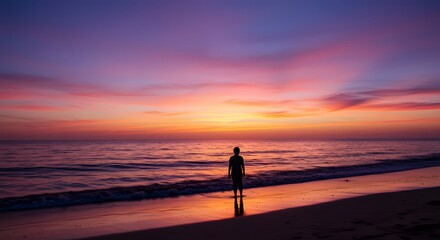 Silhouette of a person standing on a beach, watching the colorful sunset over the ocean.