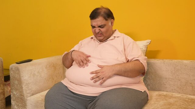 Unhappy overweight indian man suffering from Heartburn acid reflux problem . Plus size asian guy have pain in stomach and indigestion issue. Obesity and healthcare 4k