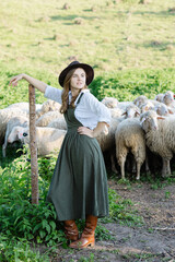 Young shepherdess leaning on a wooden pole watching over her flock of sheep