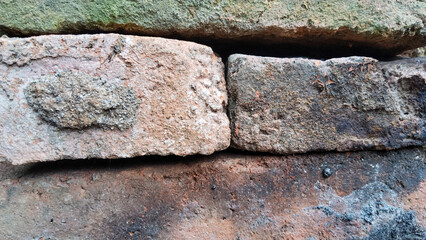 Close-up of old weathered bricks with moss and dirt texture, showcasing rustic surface and natural aging in outdoor condition