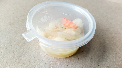 Pickled vegetables in clear plastic container on textured background, showing carrot and cucumber slices in brine
