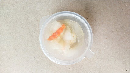 Pickled vegetables in clear plastic container on textured background, showing carrot and cucumber slices in brine