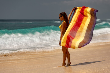 Young tanned girl in a swimsuit and pareo walks along sandy beach of a tropical sea in Thailand,...