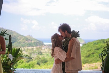 Outdoor wedding ceremony with ocean and green hills in the background. Bride in white dress and...