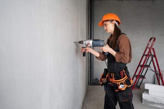 Builder worker using drill perforator making hole in wall at construction site
