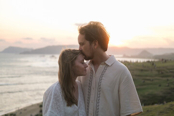 Young woman and man kissing against sunset in nature. Honeymoon, couple in love after wedding....