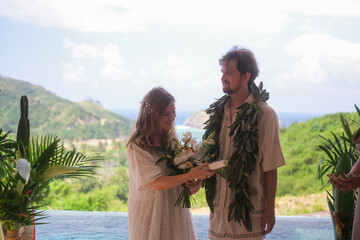 Outdoor wedding ceremony with ocean and green hills in the background. Bride in white dress and...
