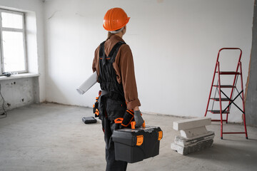 Female repair worker in helmet holding toolbox and blueprint during home or apartment renovation