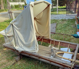 A weathered wooden cart features a beige canopy, partially draped. The cart rests on green grass...