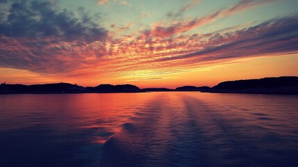 Vibrant sunset over calm water, reflecting fiery hues in the sky and sea. Silhouetted islands on the horizon complete the serene scene