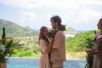 Outdoor wedding ceremony with ocean and green hills in the background. Bride in white dress and...