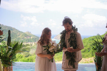 Outdoor wedding ceremony with ocean and green hills in the background. Bride in white dress and...