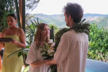 Outdoor wedding ceremony with ocean and green hills in the background. Bride in white dress and...