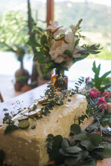 On a table decorated with flowers there is a large cake covered with white cream, fruits. Outdoor wedding ceremony. Wedding table decor for guests at an outdoor ceremony in tropical style.