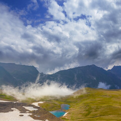 small lake in green mountain valley bowl in dense mist and clouds