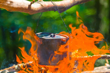 closeup touristic cauldron on a fire, summer camping cooking scene