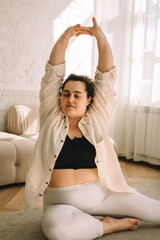 A young curly-haired plus-size woman stretches at home.Healthy lifestyle.